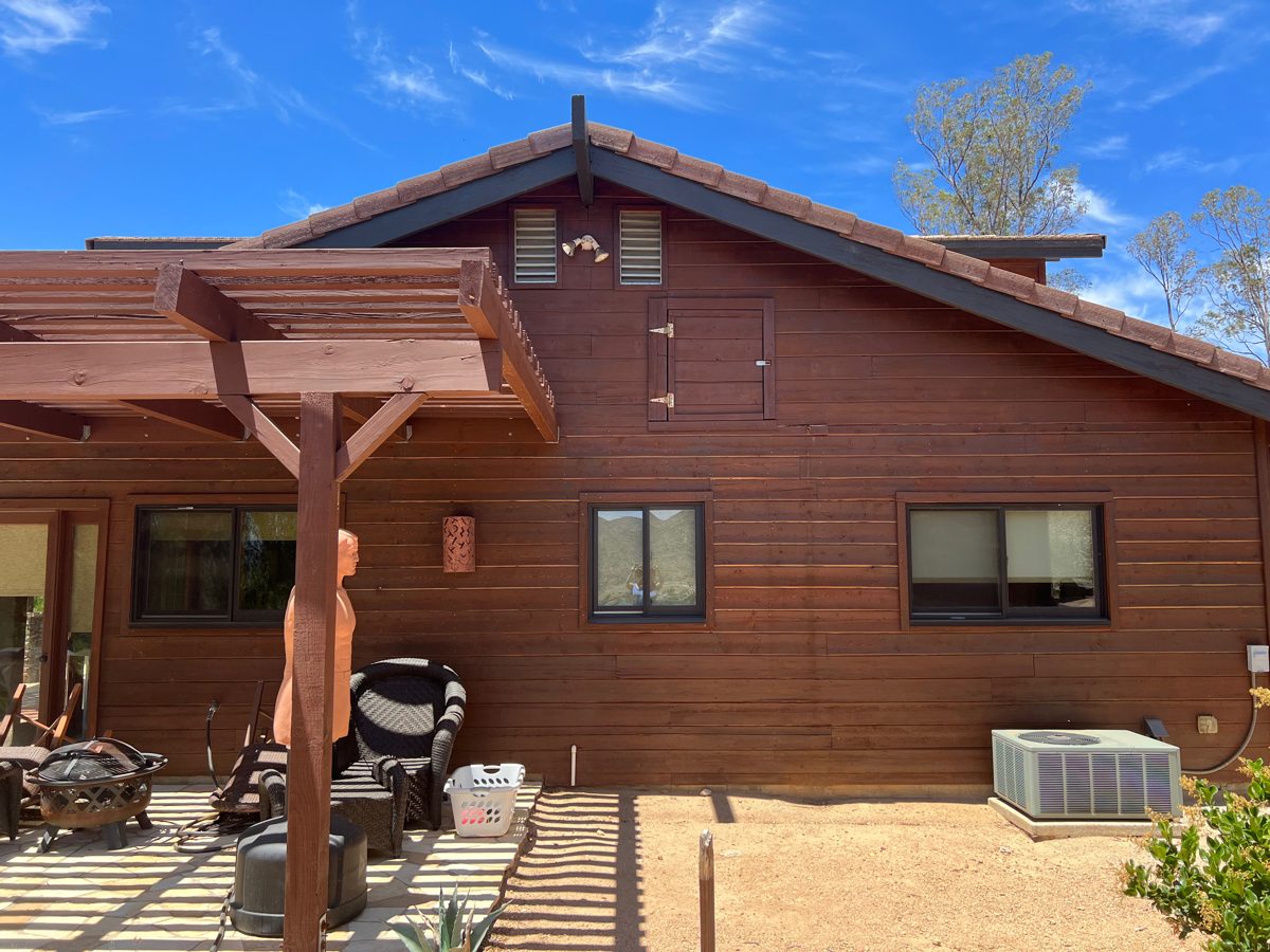 Back of a wood-sided home with stained siding and pergola